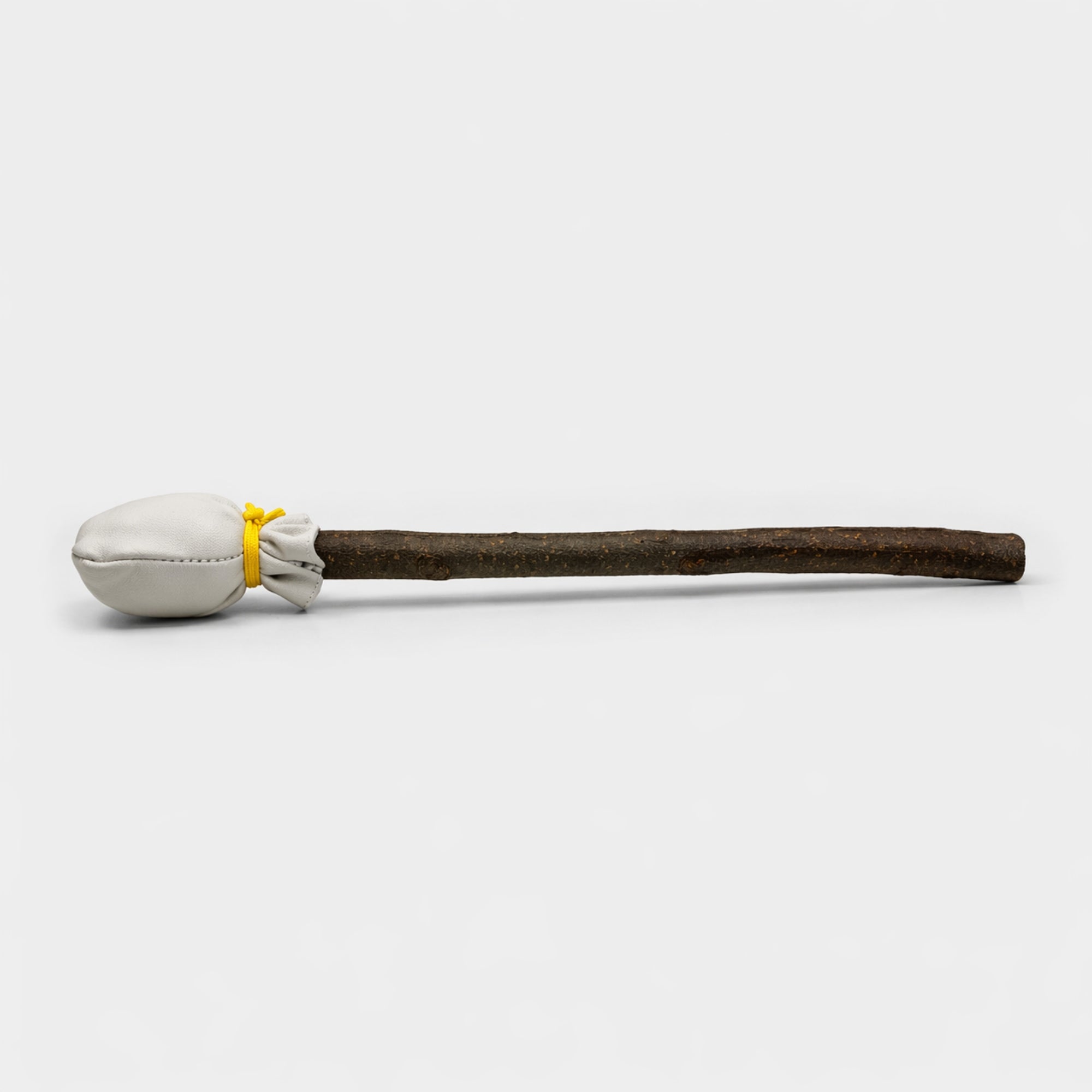 handcrafted shamanic drum beater with white fabric head on light grey studio background