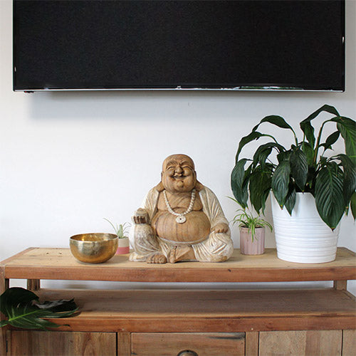 Large laughing buddha sitting next to singing bowl and plants