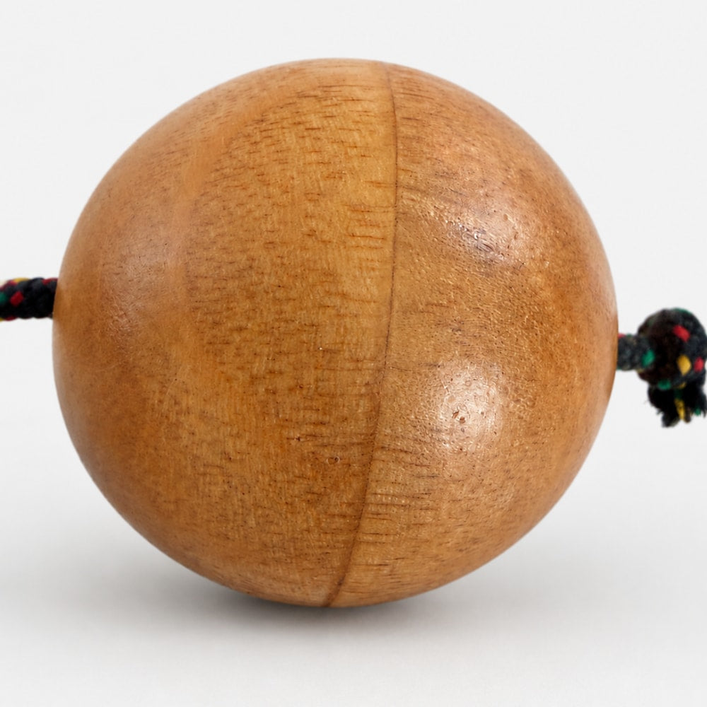 Close up of wooden kashaka ball with rope on a light grey studio background
