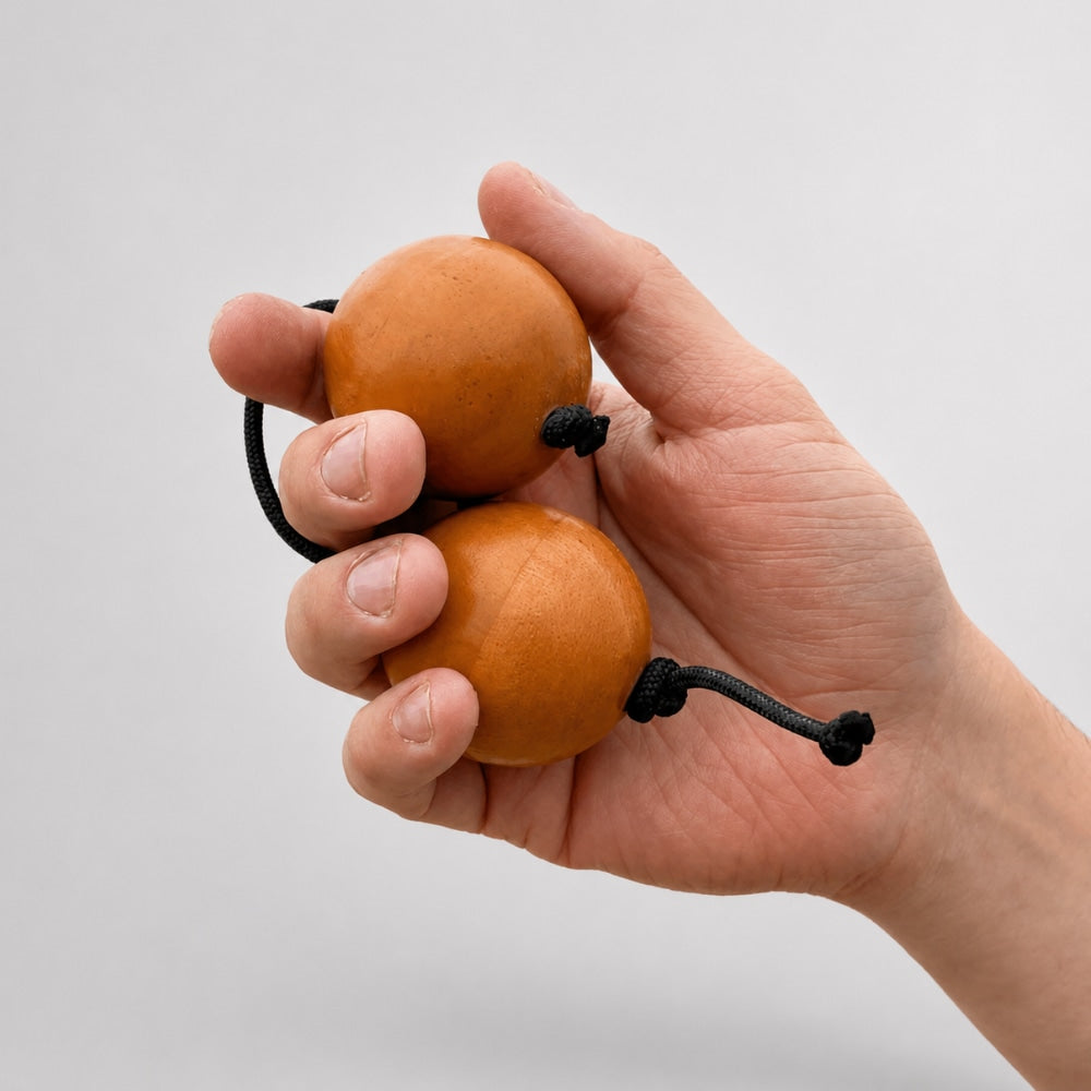 Hand holding wooden kashaka with a light grey studio background